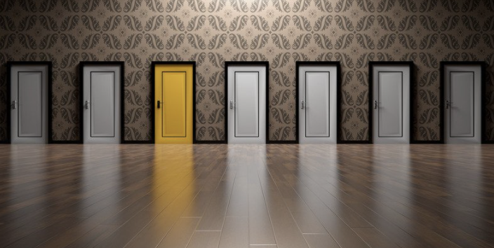 Image of seven closed doors. All are white except the one third in from the left that is yellow. 